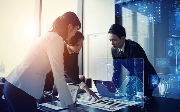 Three businesspeople in discussion around two laptops