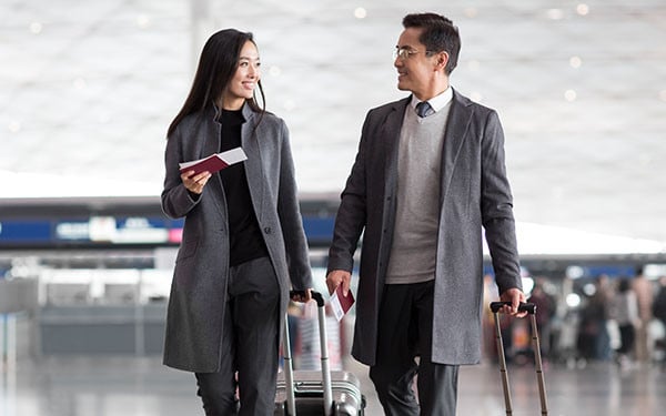 Businesspeople with passports in hand pulling suitcases in an airport lobby