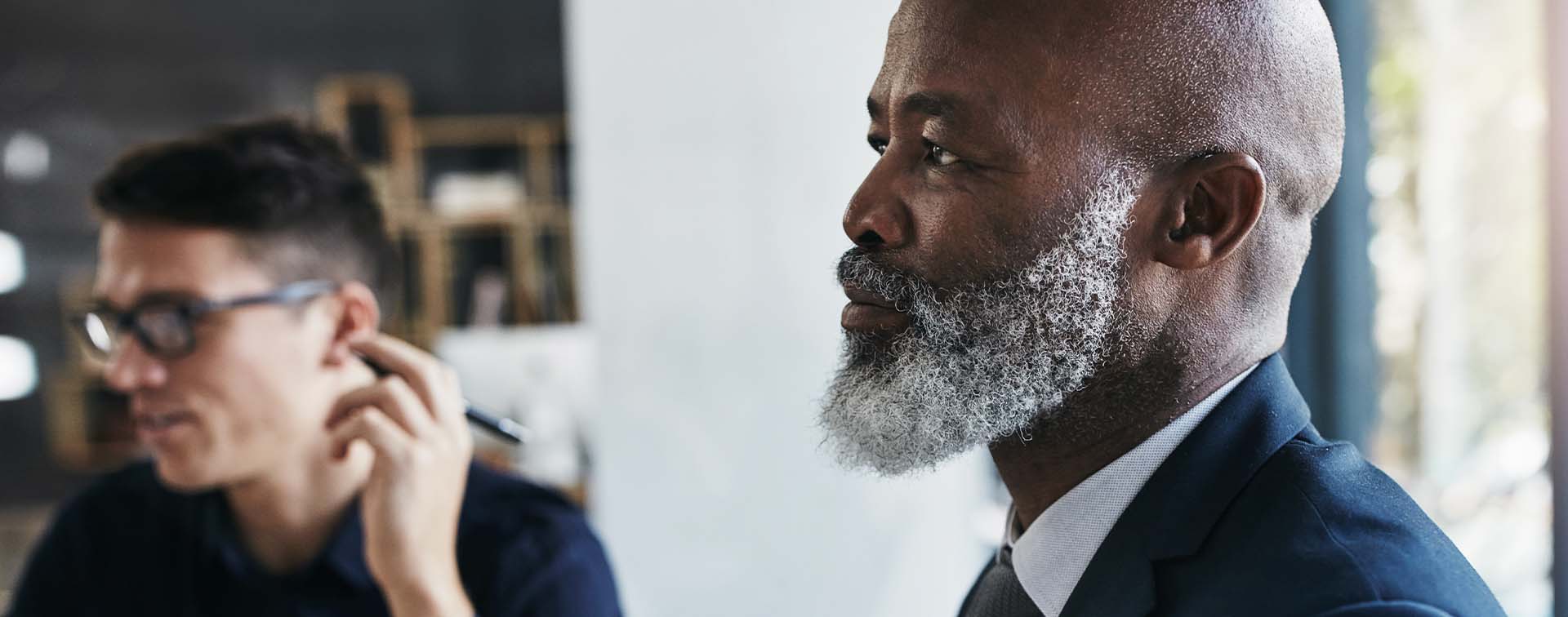 A businessman looking ahead with another man in the background holding a pen