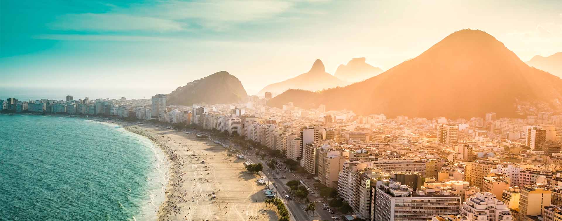 Aerial view of a populated shoreline with a city beside it and mountains in the background.