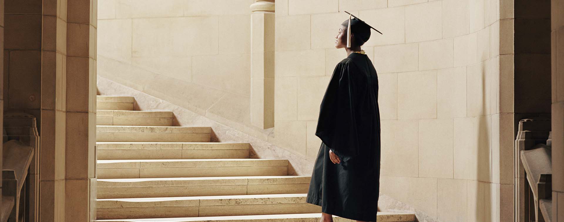 Women wearing graduation cap and gown, ascending staircase, rear view